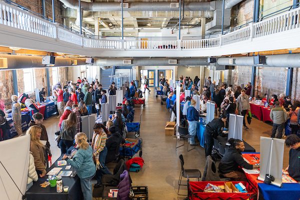 Crowds of community members gather at tables and booths during a Community Fair.