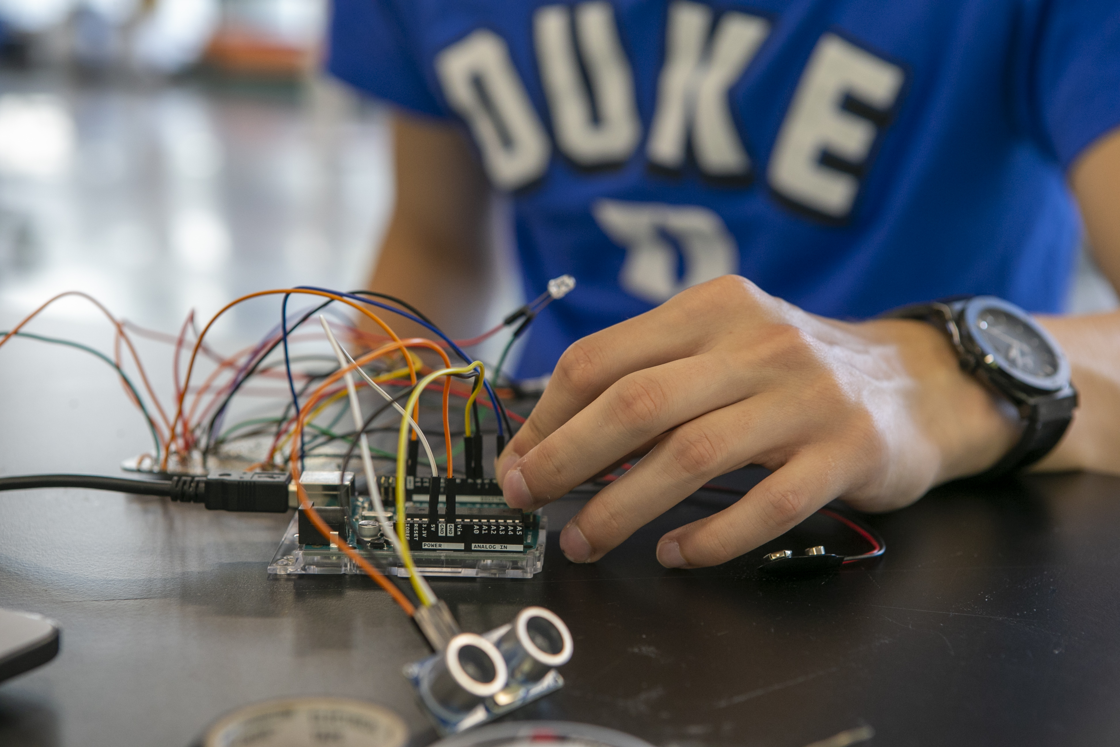 Student wearing a Duke shirt works with colorful wires on a circuit board during a STEM project.